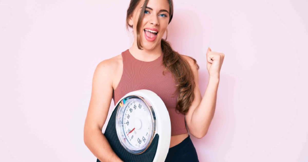 woman in activewear holding a scale celebrating her weight loss success in St. Louis, MO